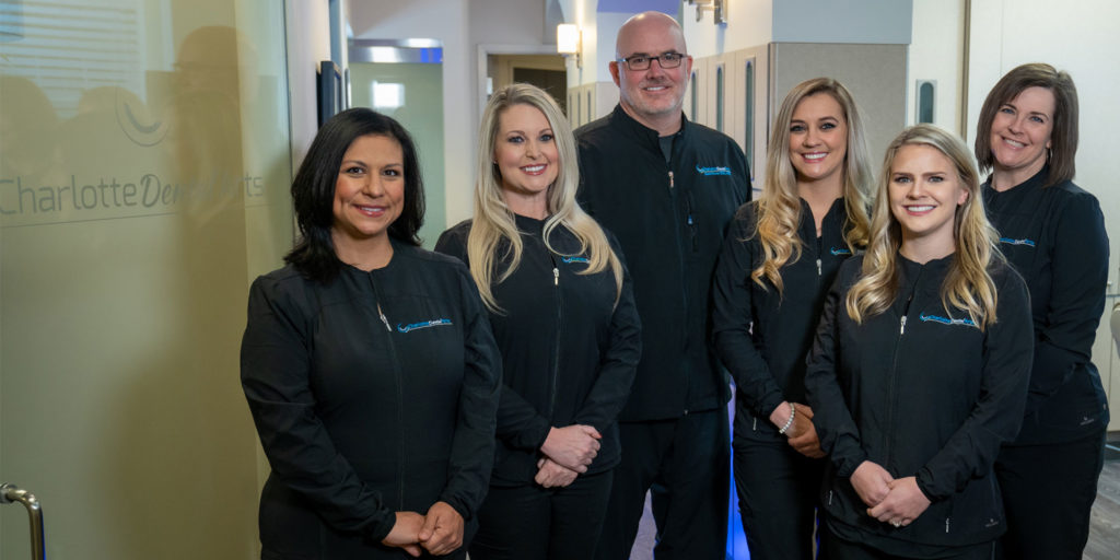 Charlotte dental arts dental team posing for picture in office in black jumper uniforms