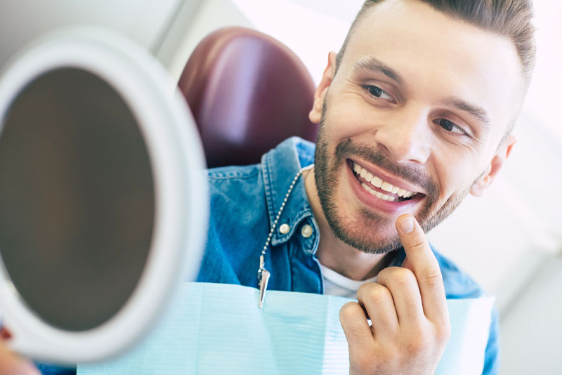 a picture of a patient happily pointing at his new smile in the mirror after he has gotten his dental veneers bonded onto his natural teeth.