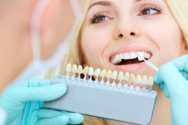 a picture of a patient smiling as the doctor is placing her custom made porcelain veneers on her teeth.