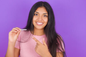 a girl holding up an invisalign clear aligner and smiling