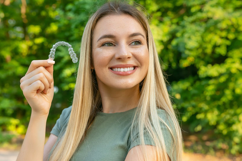 a woman holding up an invisalign clear aligner and smiling