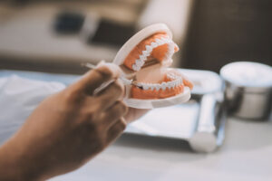 Dentist pointing with pen at dental implant using anatomical model of human jaw during consultation in dental clinic explaining to patient treatment procedure.