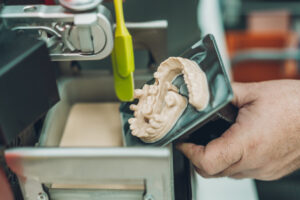 Close-up view of a hand of a caucasian adult man using a spatula to collect leftover resin from a 3D dental printer in a dental laboratory specialising in the creation of porcelain crowns